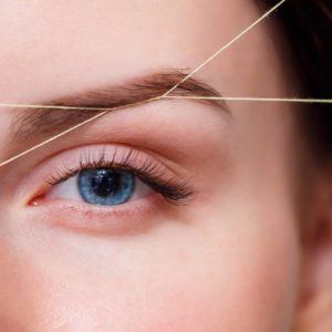 Cosmetologist plucks client eyebrows by thread. Close up